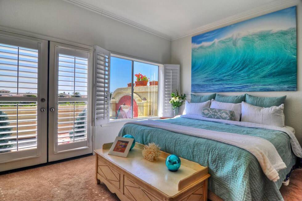 Bedroom with ocean-inspired art, teal bed and white plantation shutters