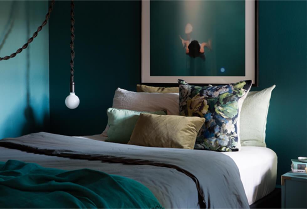 Dark, moody teal bedroom with grey bedding and simple lighting.
