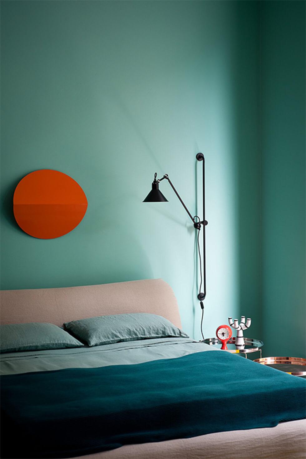 Teal bedroom with contrasting circular orange wall art and teal bedding