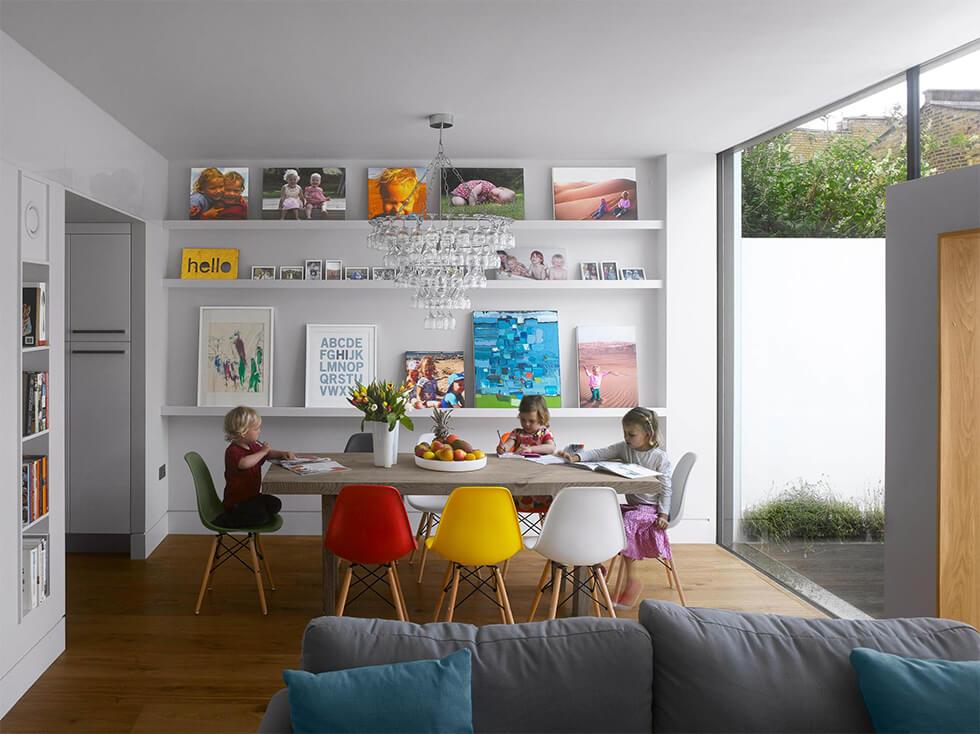 Open plan dining room with colourful chairs and open shelves with art displayed