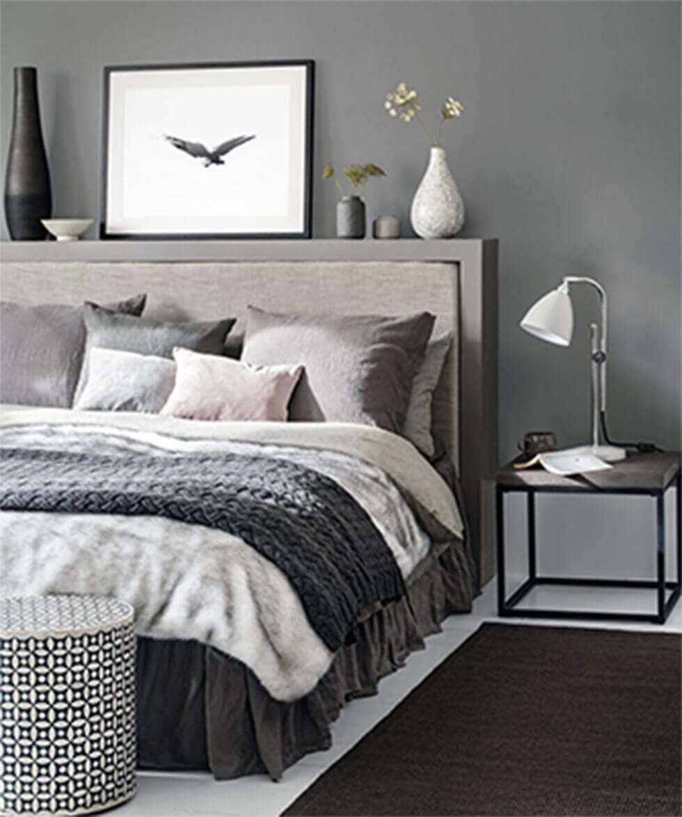 Grey bed layered with pillows, a blanket, and a throw.