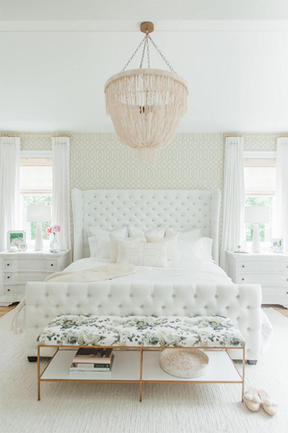 All-white bedroom with tufted headboard and beaded chandelier.